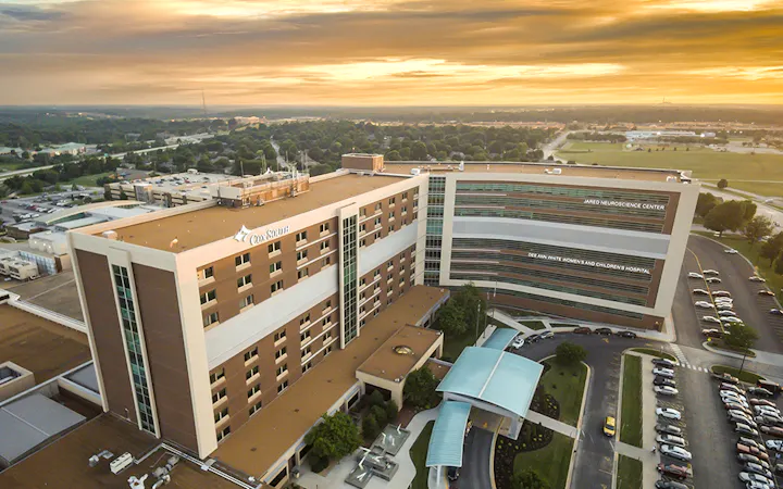 Aerial view of the Cox South hospital complex at sunset, with connected buildings and a parking lot.