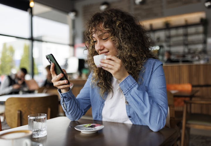 Woman sitting at a coffee shop drinking coffee and looking at her phone