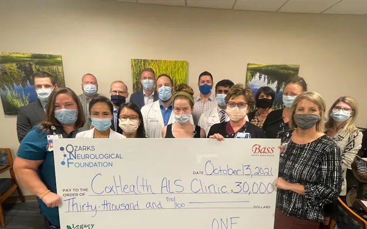 A group stands for a check presentation benefiting the CoxHealth ALS Clinic.