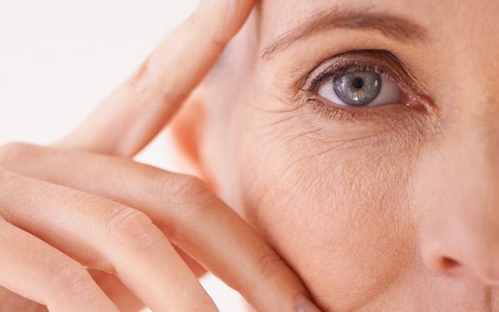 An older woman leans on her hand and looks directly into the camera.