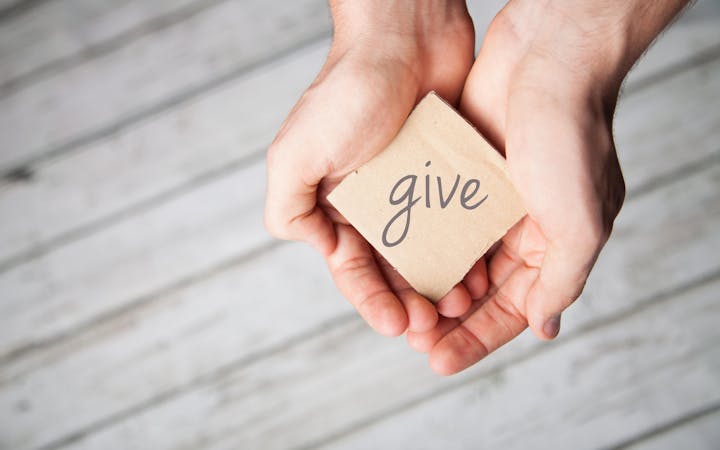 Hands holding a piece of paper that says give.