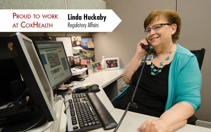 Linda Huckaby, Regulatory Affairs, on the phone at a desk with a computer and CoxHealth banner.