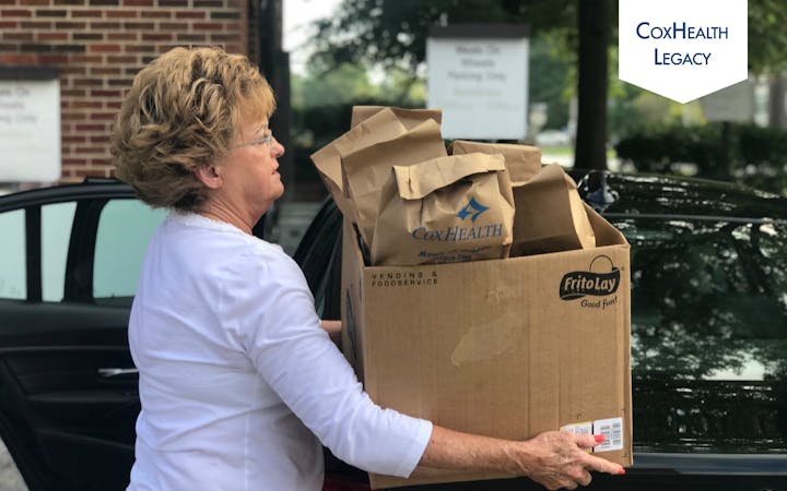 A woman prepares to put Meals on Wheels deliveries in her car.