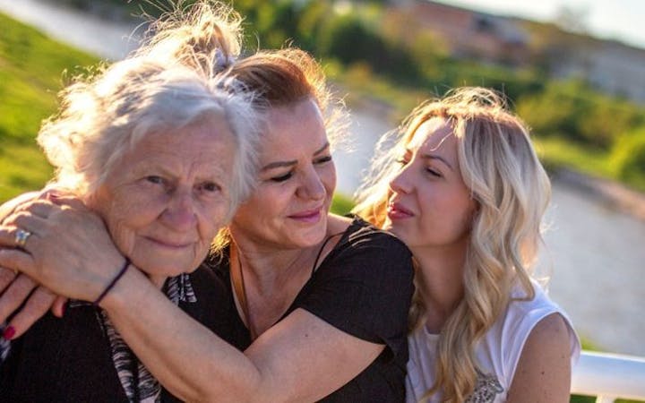 Three women ranging in age from thirties to seventies stand together outside.