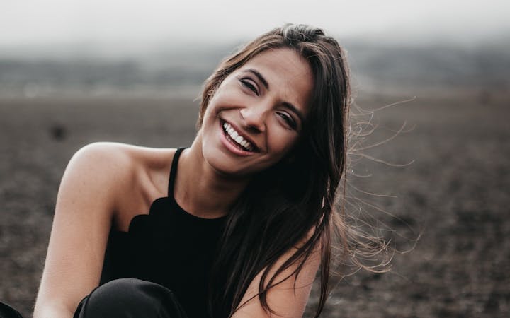 A young woman sitting outside smiles into the camera.