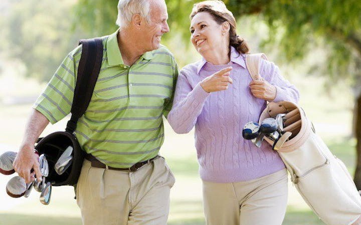 A man and a woman smile while walking on a golf course.